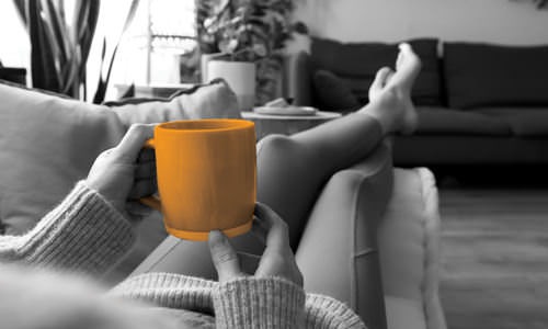 woman lays on her couch with a large mug of coffee